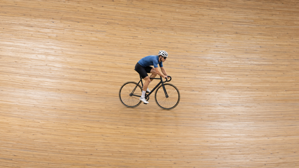 Ciclista con casco y maillot azul sobre una bicicleta de pista en un velódromo de madera